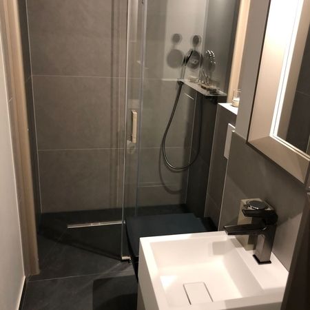 Moderne Dusche mit Glasabtrennung und dunklen Fliesen