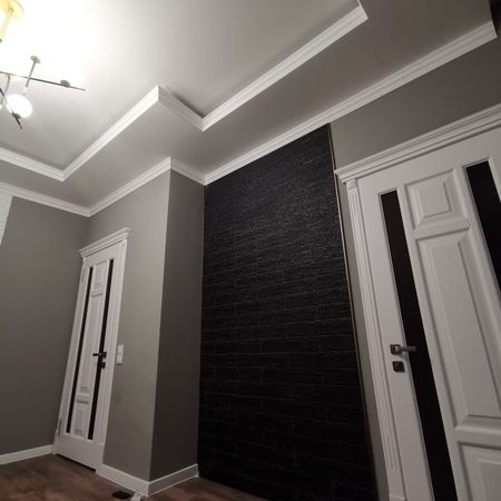 Renovierter Wohnraum mit hochwertiger Deckenverzierung und dunkler Akzentwand